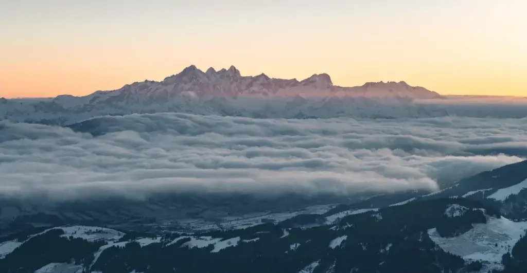 A breathtaking view of the snow-covered mountains in Salzburg during winter, with clouds gently hovering over the peaks, creating a serene and picturesque atmosphere.