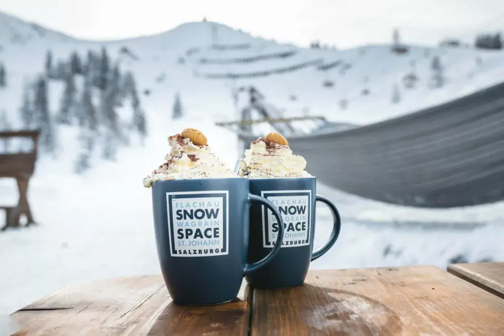 A cozy winter scene in Salzburg, featuring a coffee cup placed against a backdrop of snowy landscapes, capturing the warmth and comfort of a winter break in the Snow Space region.