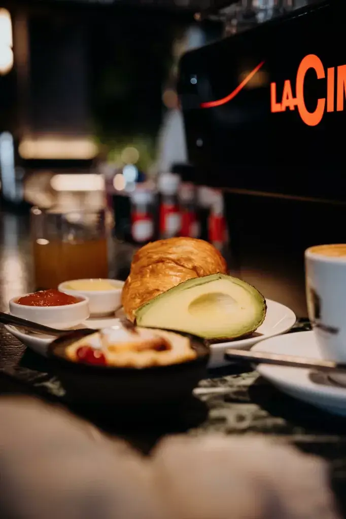 Breakfast at Gentle Hide on the bar counter, featuring a cup of coffee, creamy avocado slices, and a flaky croissant, all arranged for a delicious and satisfying morning meal in a stylish setting.