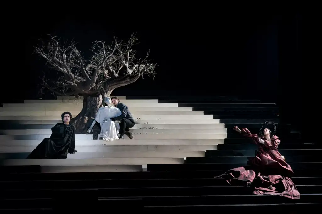 The image showcases a scene from the 2025 Mozart Week performance of *L'Orfeo*, directed by Rolando Villazón. Captured by Werner Kmetitsch, the photo features a dramatic moment from the opera, highlighting the cast, staging, and intricate costumes, creating an emotional and theatrical atmosphere.