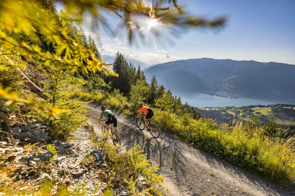 Biking with an amazing view over the lakes and mountains of Salzburger Land, as the path winds through lush green landscapes. The clear blue lakes and towering snow-capped peaks provide a breathtaking backdrop, making for a memorable and scenic cycling adventure.