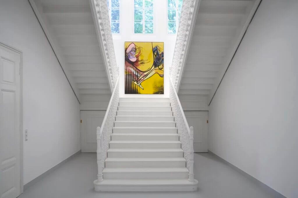 Vibrant abstract painting on a white staircase wall in a Salzburg art space.