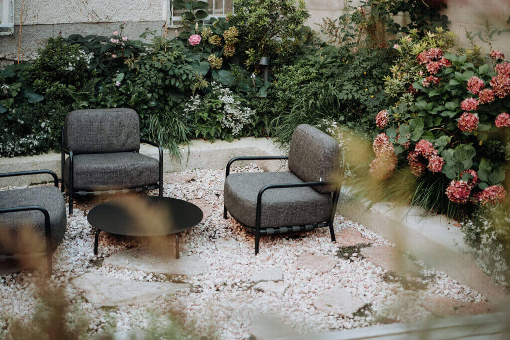 Cozy garden sanctuary with gray chairs and a black table surrounded by lush greenery.