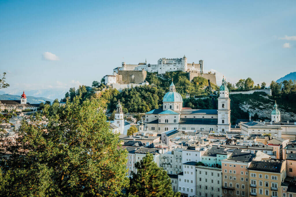 Salzburg cityscape with Hohensalzburg Fortress, domes, and green trees