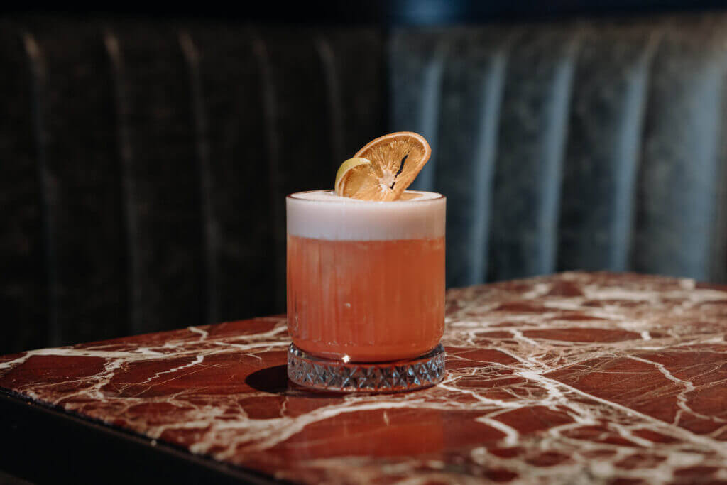 A pink aperitif cocktail with a frothy top and dried orange garnish at Hide Bar.