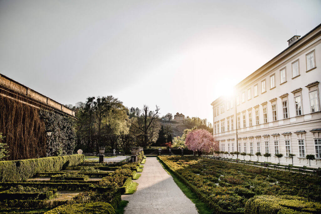 Schloss Mirabell gardens in Salzburg with manicured hedges and a historic building.
