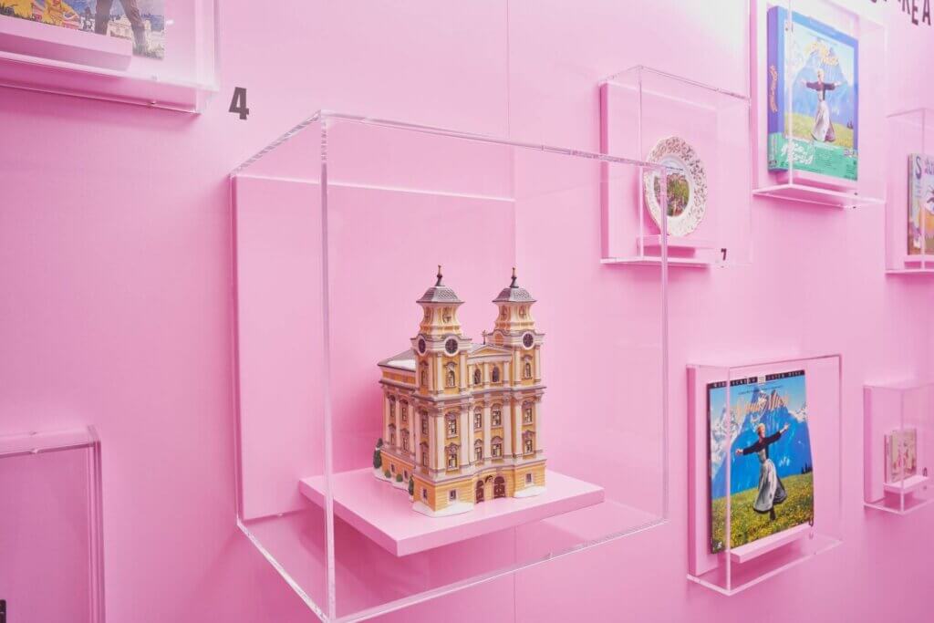 Miniature church model displayed in a clear case on a pink wall.