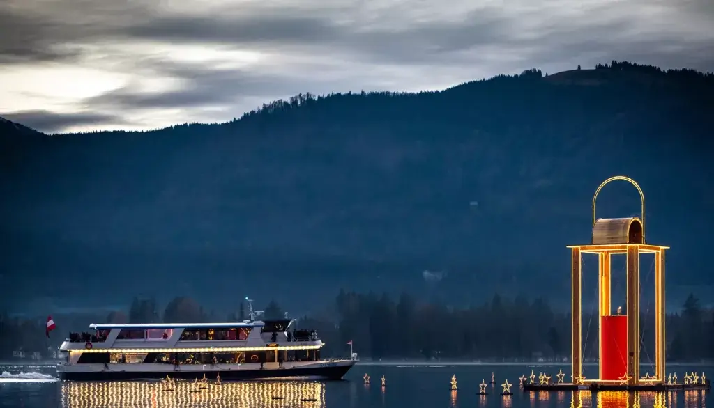 A festive Christmas ship on Lake Wolfgangsee during Advent, decorated with holiday lights and surrounded by the tranquil, snowy winter landscape. The scene captures the cozy, festive spirit of the season, with the lake reflecting the twinkling lights from the ship.